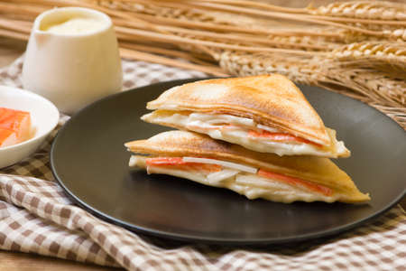 Sandwich stuffed with salad sauce and crab stick in black dish on wooden table.の写真素材
