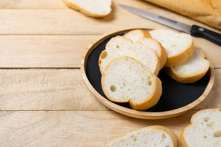 Sliced baguettes on wooden dish with knife on the wooden table.の写真素材