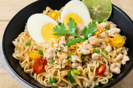 Bowl of instant noodle with minced chicken and boiled egg on wooden table.の写真素材