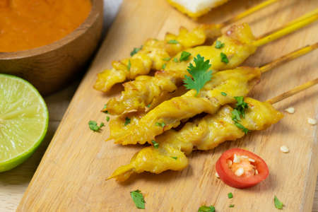 Grilled chicken satay on skewers with toast and bowl of sauce on the wooden table.の写真素材