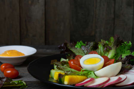 Fresh salad with boiled egg in black dish on wooden table, Tomato and Radish.
