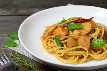 Spaghetti with sausages and fried basil in white dish on the old wooden table.の写真素材