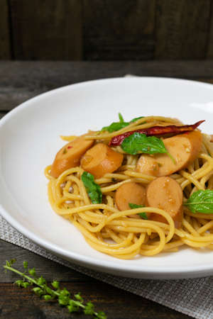 Spaghetti with sausages and fried basil in white dish on the old wooden table.の写真素材