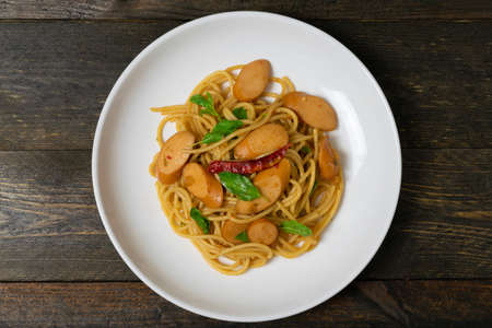 Spaghetti with sausages and fried basil in white dish on the old wooden table.の写真素材