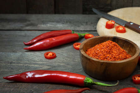 Cayenne in small bowl with chili on wooden table.