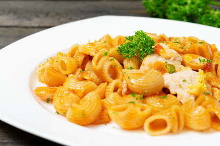 Macaroni in tomato sauce with sausage and fried egg in white dish on wooden table.の写真素材