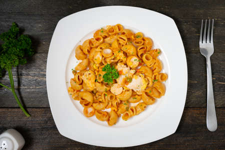 Macaroni in tomato sauce with sausage and fried egg in white dish on wooden table.の写真素材