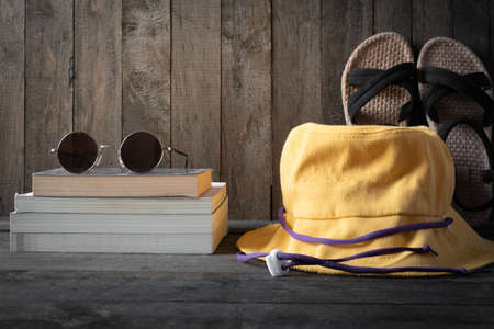 Yellow hat with sunglasses, sandals and book on wooden table.の写真素材