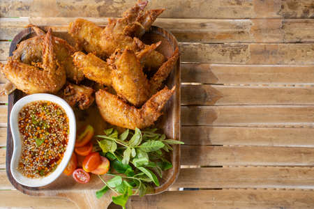 Fried wing chicken with sauce in wooden dish on bamboo table.の写真素材