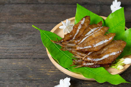 Fried dried fish on mango leaf in wooden dish on wooden table.の写真素材