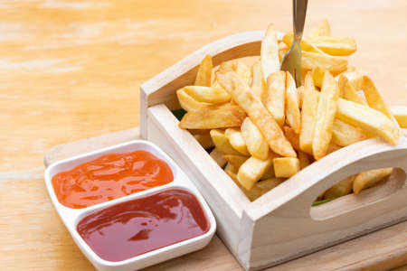 French fries in wooden tray with tomato and chili sauce on wooden table.の写真素材