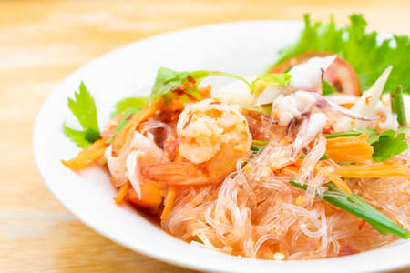 spicy vermicelli salad with seafood in white dish on wooden table.の写真素材