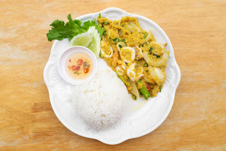Stir fried squid in curry powder with rice and fish sauce mixed chili in white dish on wooden table.の写真素材