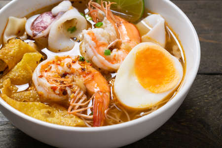 Spicy rice noodle with seafood and crispy wonton in white bowl on wooden table.の写真素材