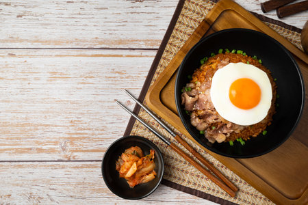 Top view of Kimchi rice with grilled brisket sliced and fried egg in black bowl on wooden table.の写真素材