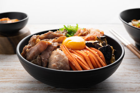 Kimchi fried rice with fried brisket and wakame seaweed and raw egg in black bowl on wooden table,(bibimbap).の写真素材