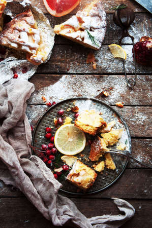 Pieces of apple pie sprinkled with powdered sugar. Homemade cut apple cake decorated slices of lemon and green spruce branches on a wooden background. Rustic dark food style.の写真素材