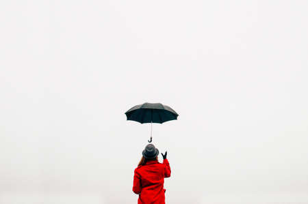 Active lifestyle concept. Girl in a red jacket and pants standing backwards with a black umbrella in the handsの写真素材