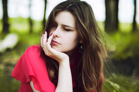 Young beautiful girl in a pink coat and pink short dress boots resting on a spring green meadow on a background of green grass. Beautiful Young Woman Outdoors. Enjoy Nature.の写真素材