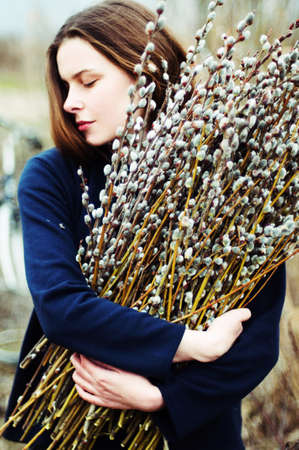 Portrait of a beautiful young girl with a huge armful of willow in hands. Young woman gardening.の写真素材