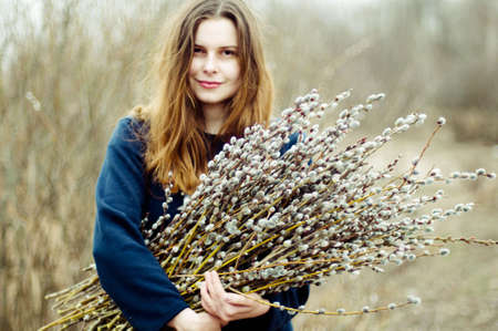 Portrait of a beautiful young girl with a huge armful of willow in hands. Young woman gardening.の写真素材