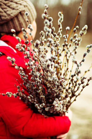 Portrait woman in a red jacket with a huge armful of willow in hands. Young woman gardening. Portrait of a girl in nature. Girl with willow outdoors.の写真素材