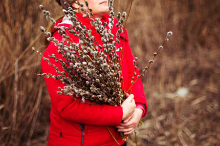 Portrait woman in a red jacket with a huge armful of willow in hands. Young woman gardening....