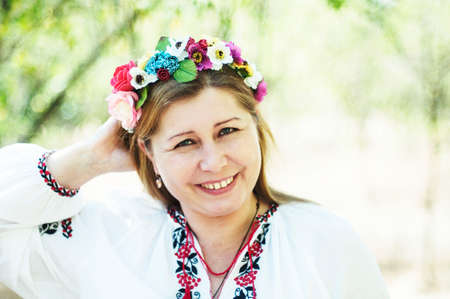 Young beautiful woman posing in 40 beautiful floral wreath on her head and an embroidered shirt on...
