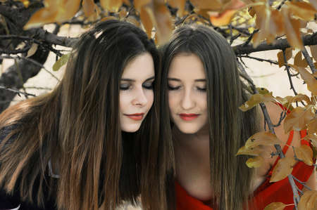 Portrait of beautiful young girls dressed in ornoe and red long dress. Two girls, friends, poztruyut in spring park on background of green trees.Two young smiling friends, portrait, summerの写真素材