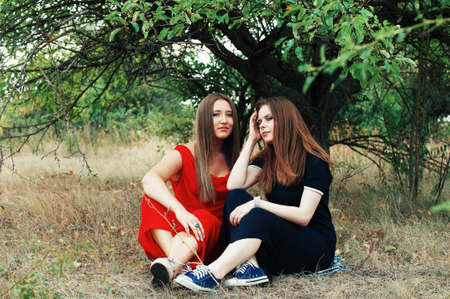 Portrait of beautiful young girls dressed in ornoe and red long dress. Two girls, friends, poztruyut in spring park on background of green trees.Two young smiling friends, portrait, summerの写真素材