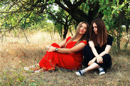 Portrait of beautiful young girls dressed in ornoe and red long dress. Two girls, friends, poztruyut in spring park on background of green trees.Two young smiling friends, portrait, summerの写真素材