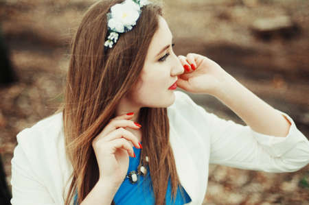 Beautiful young girl with long straight hair, light make-up in a stylish trendy business suit standing outdoors in a park on a background of trees. The girl looks into the cameraの写真素材