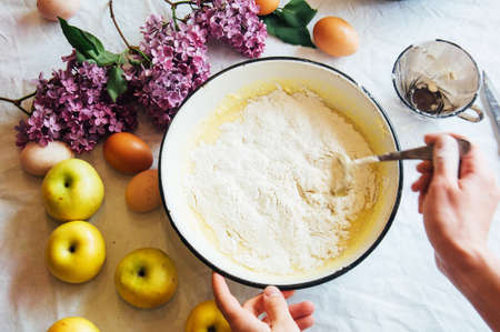 A woman prepares a pie apple tree, the ingredients for the cake: flour, egg, vanilla, sugar, milk, sour cream, soda. The girl in the kitchen. Women's hands. Preparation of Desserts for breakfastの写真素材