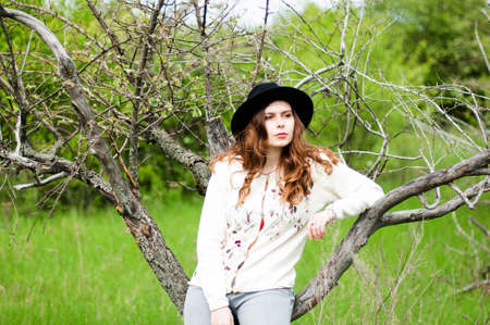 Stylish spring bohemian outfits. Wearing a white sweater and black hat in blooming garden. Beautiful...