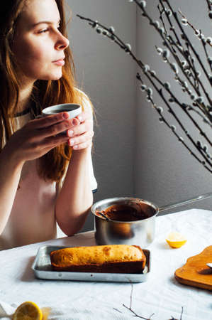 Cupcake for breakfast . Rustic  styling.  Homemade fresh-baked milk cake on the white tablecloth at a window. Country white kitchen.  The girl in the kitchen.Fresh hot coffee.の写真素材