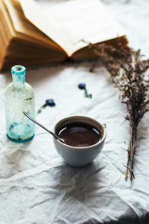 Fresh hot coffee on a pile of books on a table covered with a white cloth at the window. Still life. Rustic dark stying.の写真素材