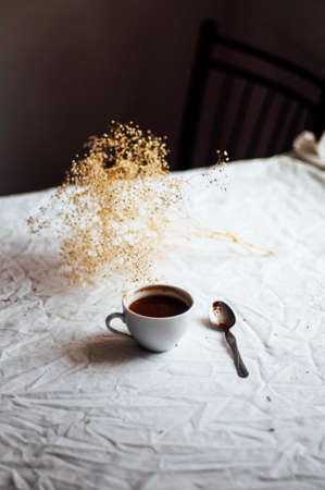 Fresh hot coffee on a pile of books on a table covered with a white cloth at the window. Still life. Rustic dark stying.の写真素材