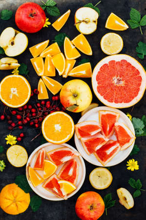Mixed festive colorful tropical and citrus fruit sliced over black table top.  Food collage on a rustic surface. Apples, lemons, grapefruit, oranges, berries. Citrus  fruits background.の写真素材
