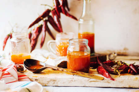 Red hot sweet chilli sauce over old white wooden background. Rustic styling. Pepper sauce  with  parsley and garlic in glass jar. Home made ketchup in a jar. Canning Marinara sauceの写真素材