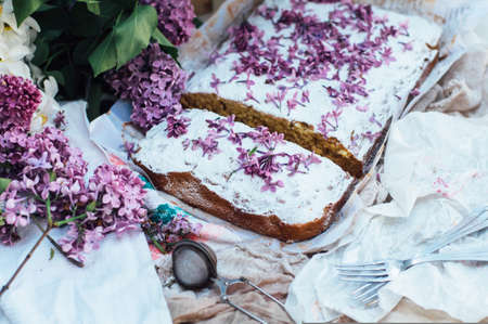Homemade delicious fresh vanilla cake with apples sprinkled with powdered sugar and decorated with flowers and branches of lilac on a white kitchen table. Dessert cake for a large family.  sweetsの写真素材