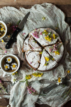 Delicious fresh homemade pie with orange zest, milk, butter, eggs. Decorated with slices of orange on a wooden background. Cake sprinkled with powdered sugar. Decorated with wild flowersの写真素材