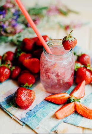 A glass of strawberry smoothie on a wooden background. Strawberry smoothie. Closeup of strawberry fruit smoothies with strawberry pieces in glass with straw. Strawberry smoothie on rustic woodの写真素材