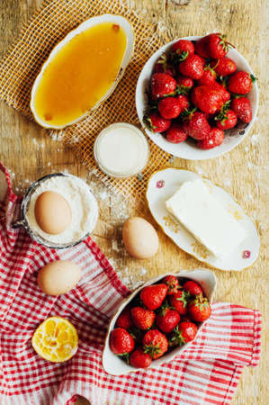 Cooking cake with fresh ingredients for preparing in cooking. Rustic dark atmosphere. Flour, eggs and fresh strawberries, cherries, butter, flour over on wooden background. Series, recipe step on stepの写真素材