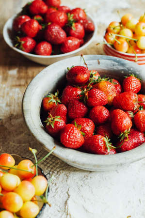 Fresh  ripe strawberries and yellow cherries laid out on the dishes. Fresh strawberries on the rustic table. Preparing jam of berries on wooden background. Top view. Strawberries jam. Rustic styling.の写真素材