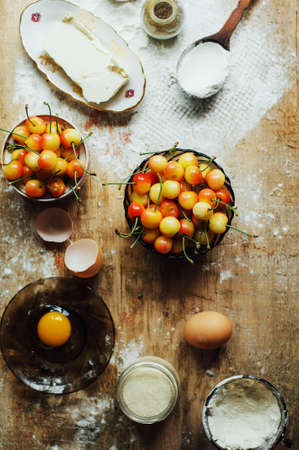 Cooking cake with fresh ingredients for preparing in cooking. Rustic dark atmosphere. Flour, eggs and fresh strawberries, cherries, butter, flour over on wooden background. Series, recipe step on stepの写真素材