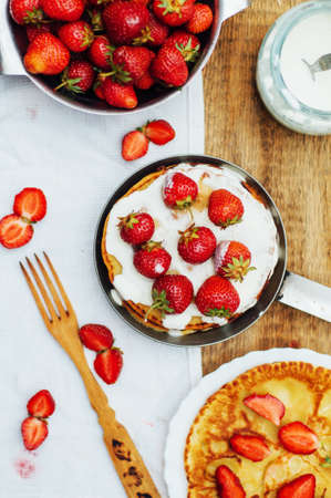 Strawberries and whipped cream  for dessert. Pancakes with  strawberries and sour cream. Stack of pancakes with fresh strawberry and balsamic glase in frying pan on wooden table. Rustic styleの写真素材