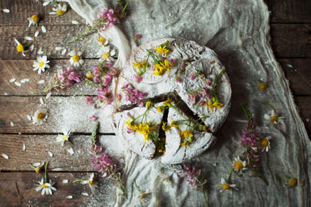 Delicious fresh homemade pie with orange zest, milk, butter, eggs. Decorated with slices of orange on a wooden background. Cake sprinkled with powdered sugar. Decorated with wild flowersの写真素材