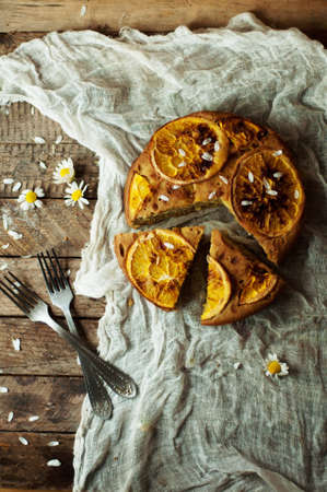Delicious fresh homemade pie with orange zest, milk, butter, eggs. Decorated with slices of orange on a wooden background. Cake sprinkled with powdered sugar. Decorated with wild flowersの写真素材