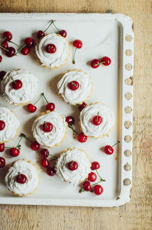 Beautiful chocolate cupcakes with white protein cream and cherry. Vanilla cupcakes with  cream frosting and a cherry on top. Cherry Cupcake Shot on wooden table. Ripe red cherries and currant muffinの写真素材