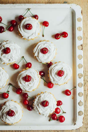 Beautiful chocolate cupcakes with white protein cream and cherry. Vanilla cupcakes with  cream frosting and a cherry on top. Cherry Cupcake Shot on wooden table. Ripe red cherries and currant muffinの写真素材